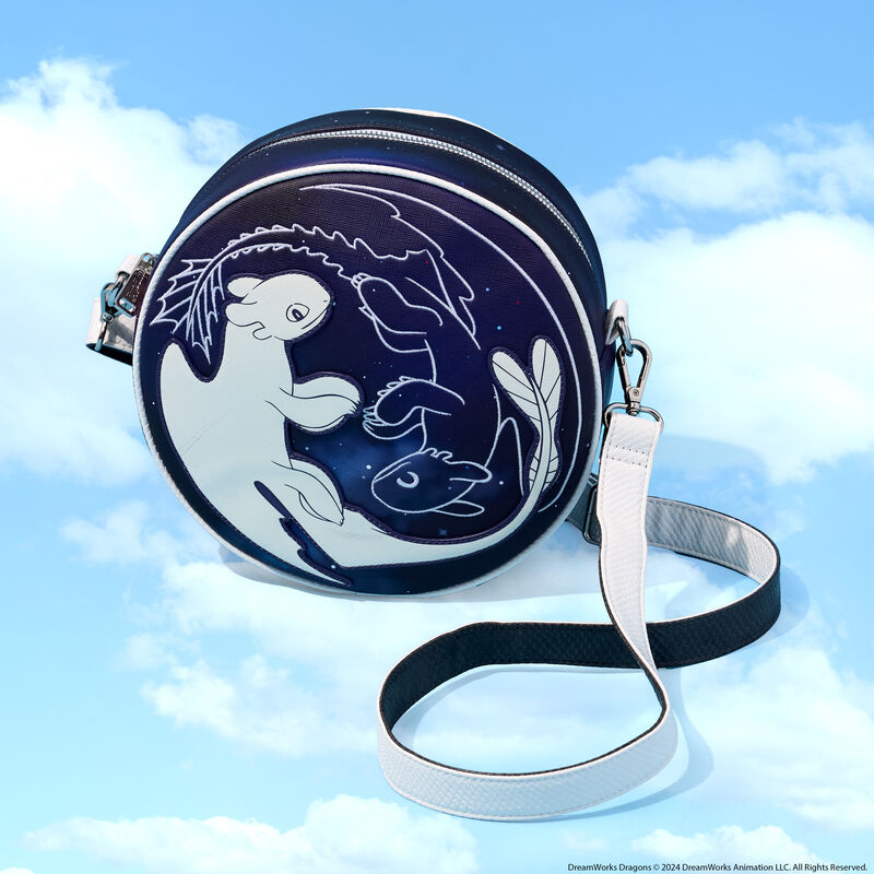 Circular Loungefly How to Train Your Dragon crossbody bag featuring Light Fury and Night Fury as a Yin and Yang type symbol against a dark background. The bag sits against a background that looks like a light blue sky with clouds.